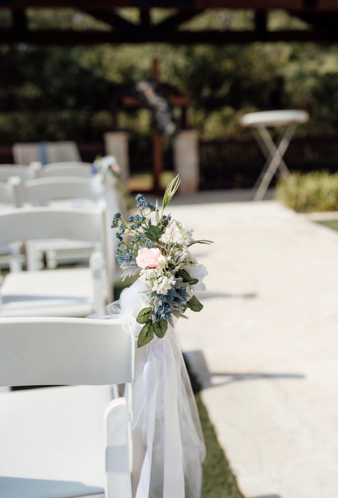 Floral arrangement along the ceremony aisle with a wooden cross beyond