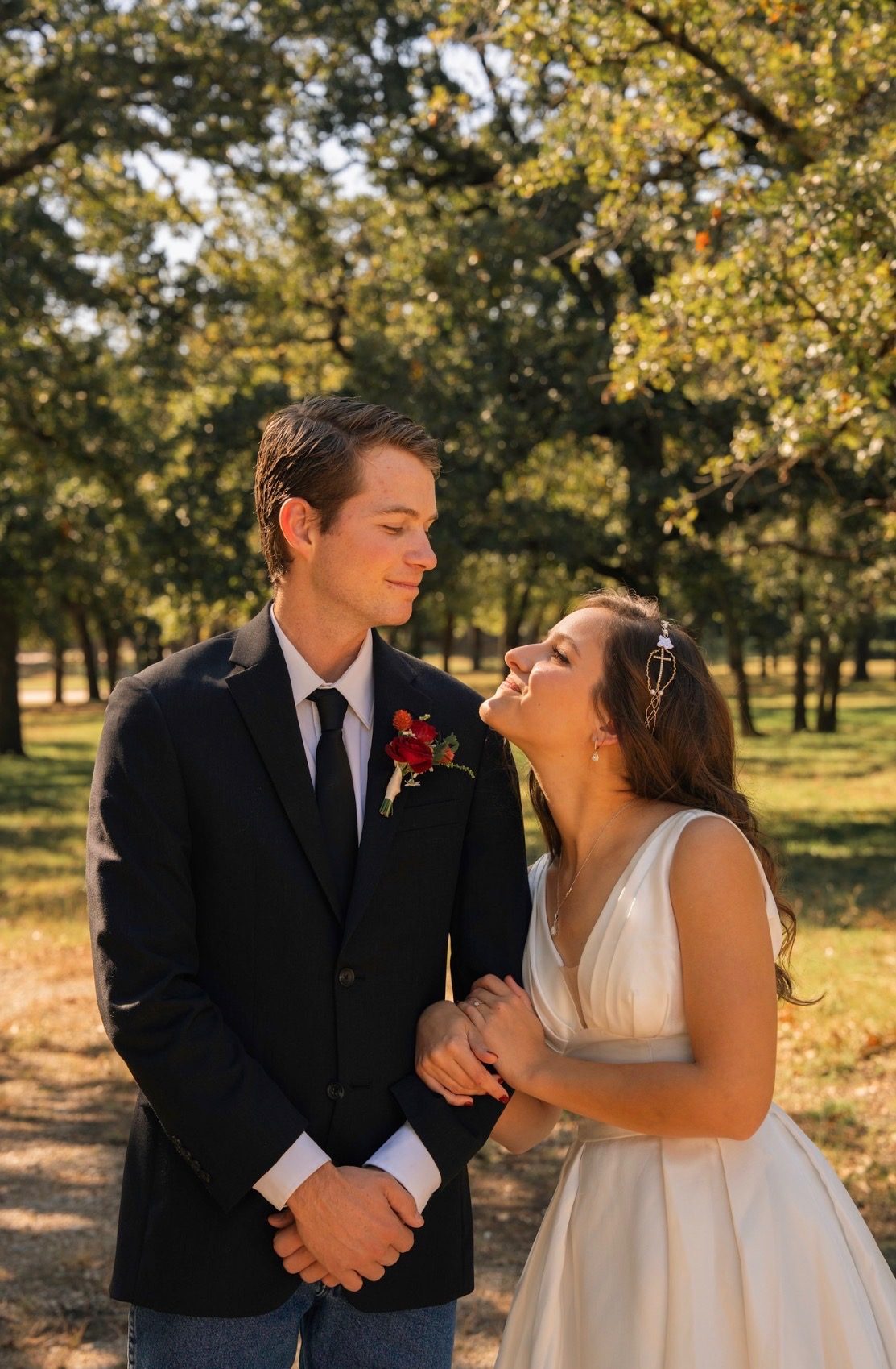 Bride and groom smiling at each other beneath autumn trees