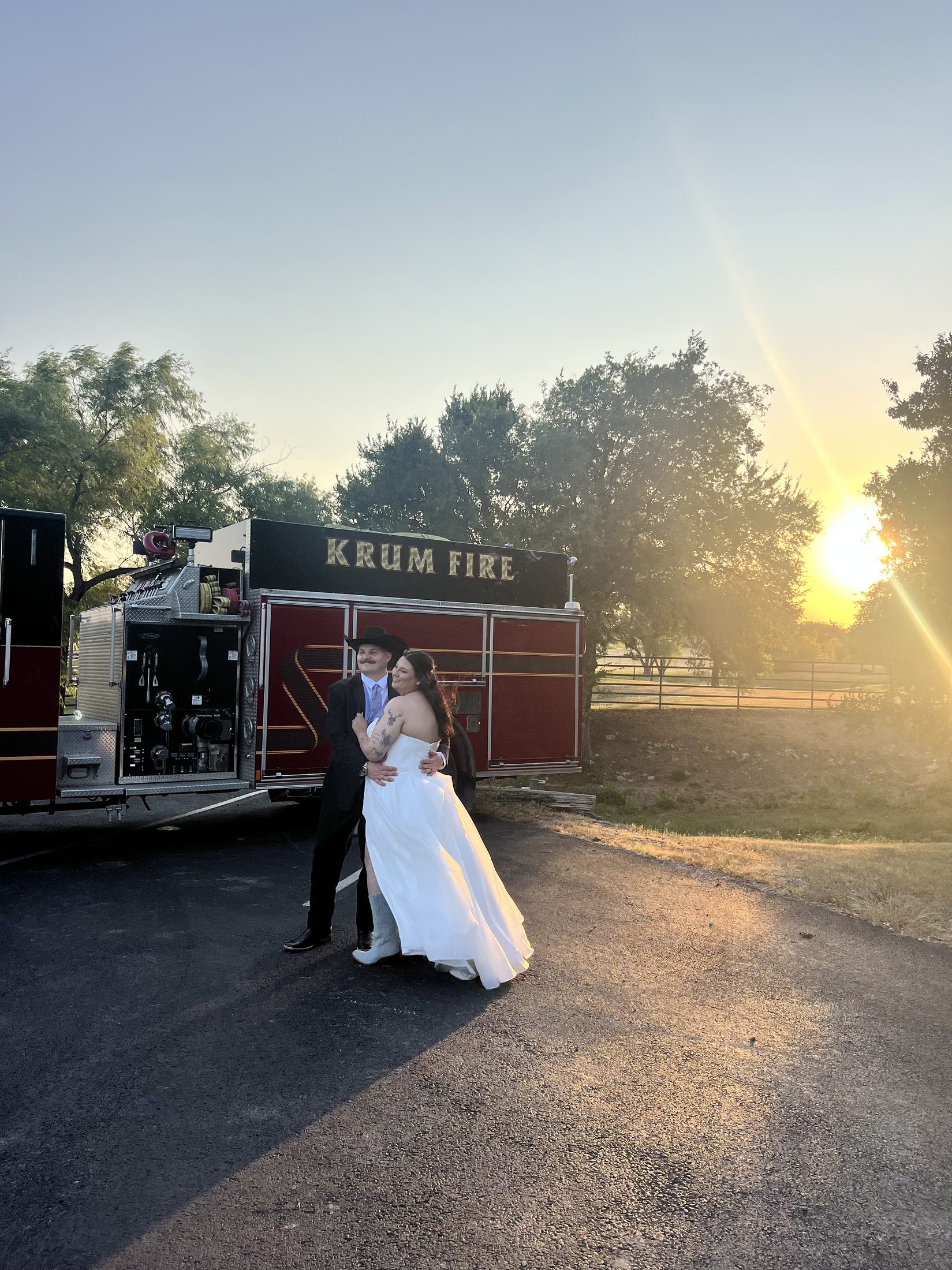 Bride and groom embracing beside a fire truck at golden hour