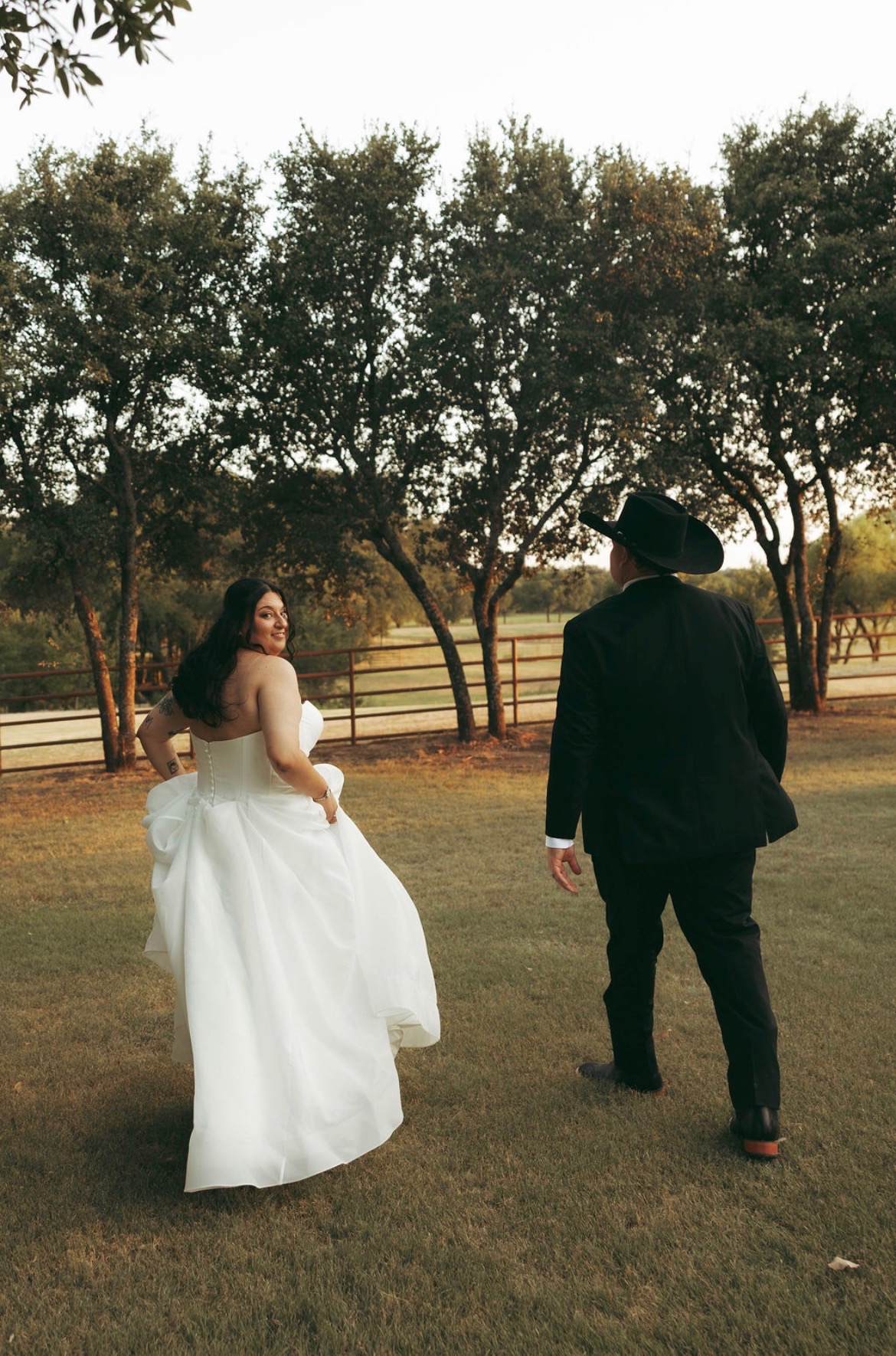 Bride glancing back at her groom in a cowboy hat during their ranch first look