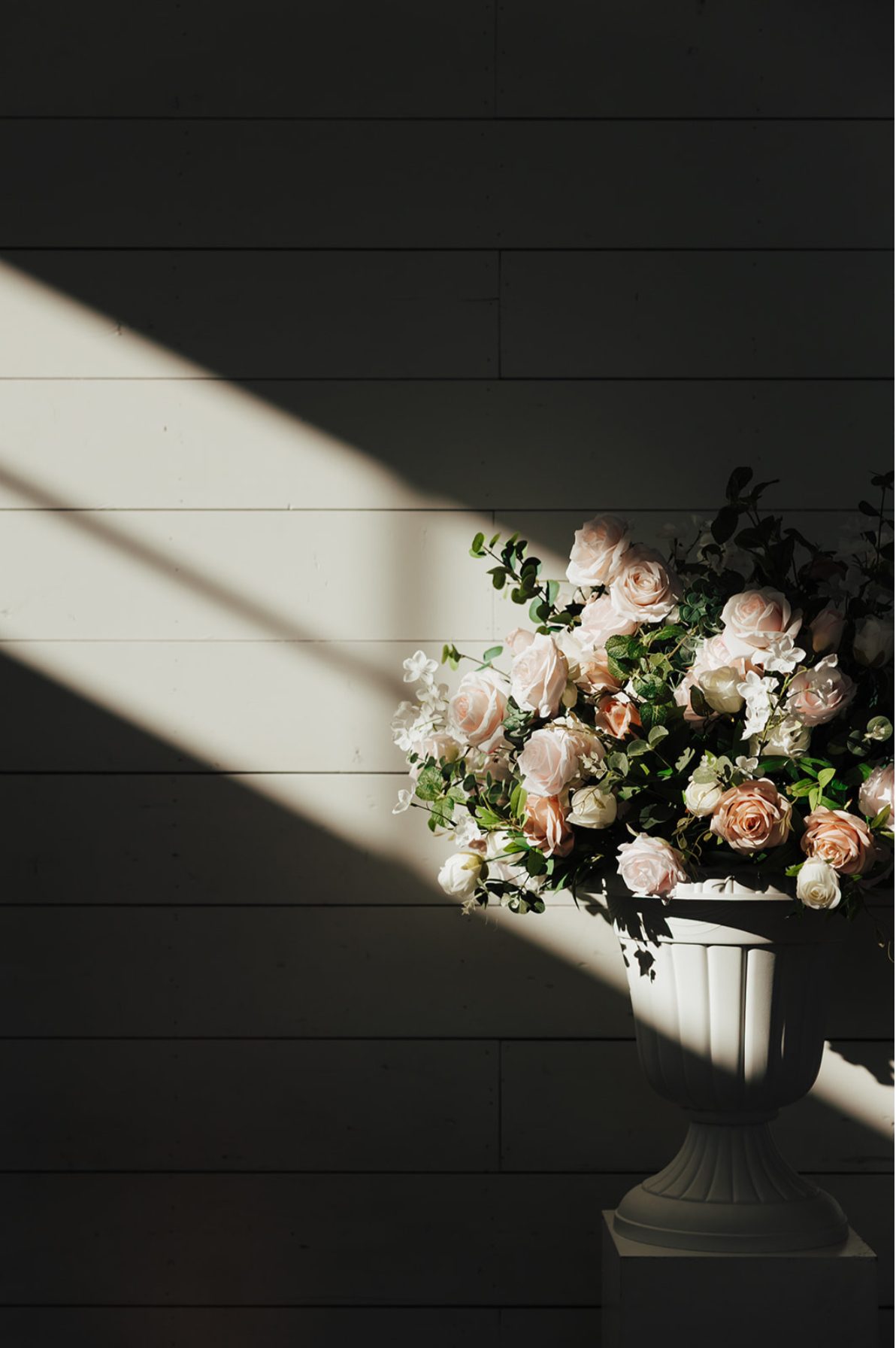 Blush florals in a white urn lit by a shaft of window light