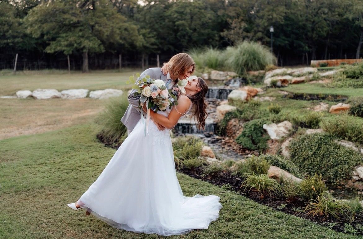 Groom dipping his bride for a kiss beside a garden waterfall