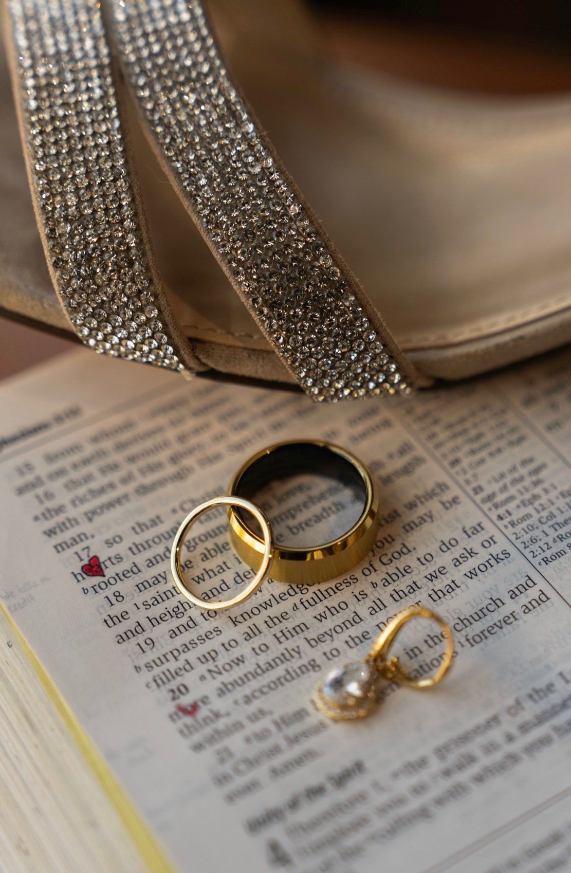 Wedding rings and earrings resting on an open Bible beside a beaded clutch