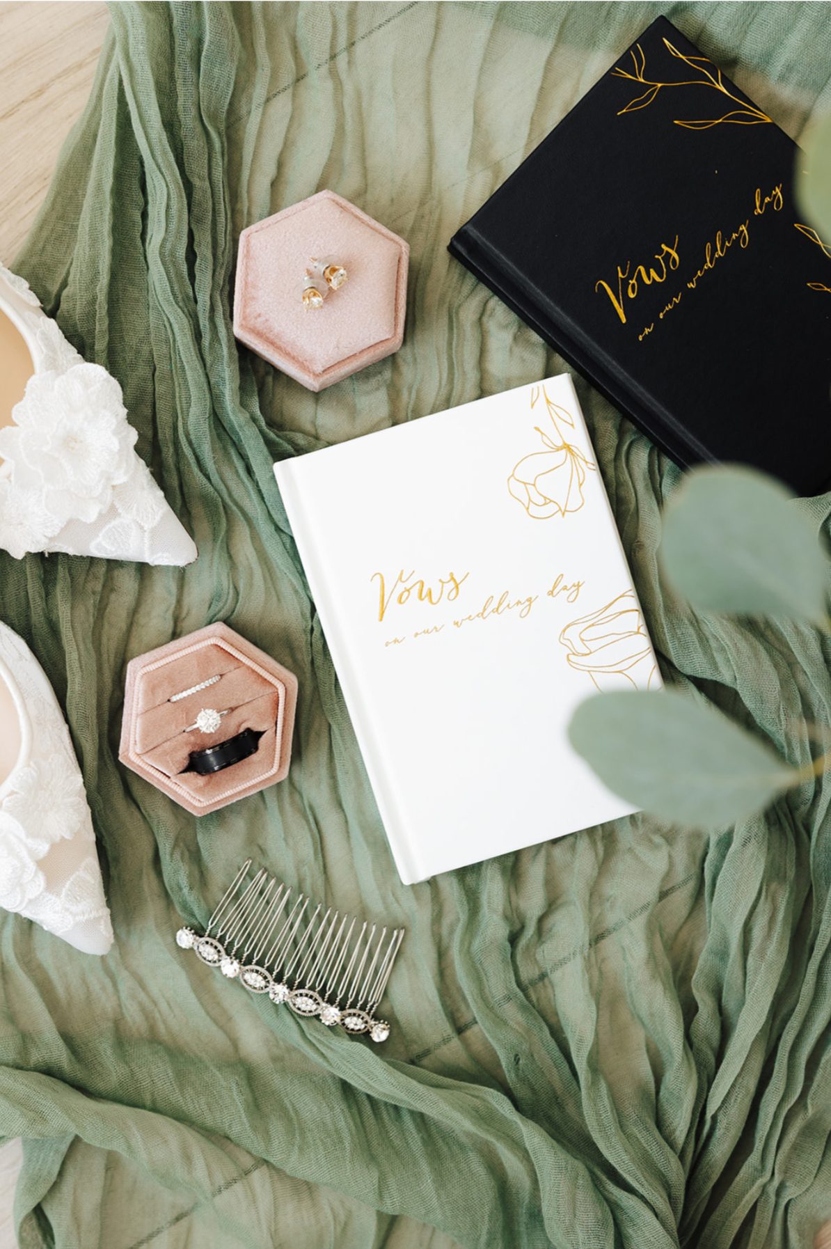 Vow books, ring boxes, and bridal shoes styled on a sage scarf